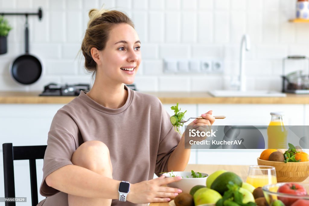 Happy woman enjoying a fresh salad in her kitchen, showcasing a healthy lifestyle and diet with a vegetarian meal.